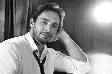 Young and handsome man sitting alone at the bar counter with a glass and a bottle. Alcoholic in the...