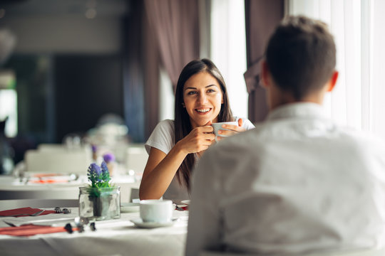 Smiling woman on a date in a restaurant,having a conversation over a meal in hotel.Cheerful female customer drinking coffee with a partner.Positive emotions,love,affection.Public place behave manners