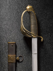 Closeup of a beautiful sword saber with scabbards against a dark background with a texture under the metal.