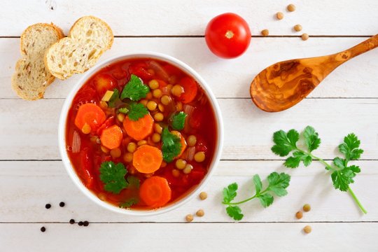 Homemade tomato, lentil soup, above scene on a white wood background