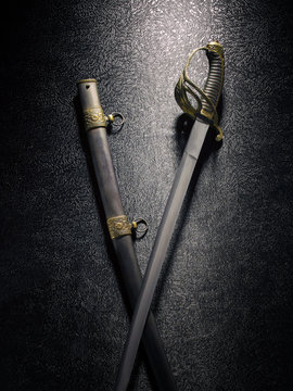 Closeup of a beautiful sword saber with scabbards against a dark background with a texture under the metal.