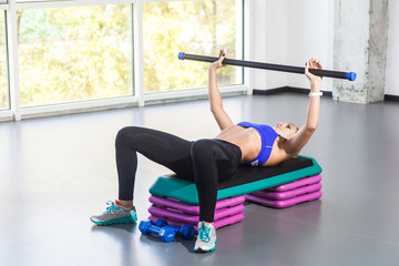 Blonde woman lie on step platform and push barbell