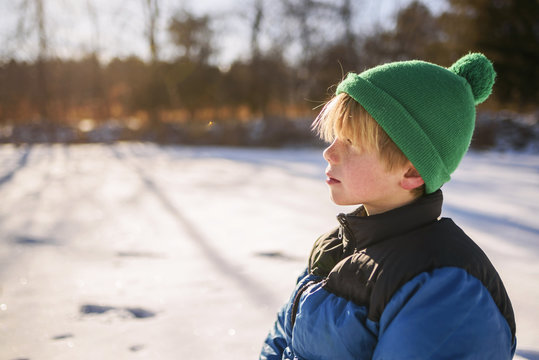 Close-up profile Portrait of a young boy wearing a woolly bobble hat standing in a snowy winter landscape