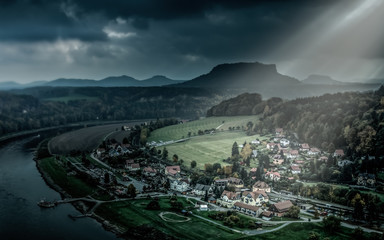 Small city in Saxon Switzerland National Park on Elbe river under sun rays breaking through the heavy clouds