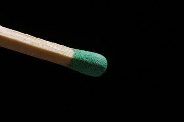 Unburnt matchstick with green head against black background