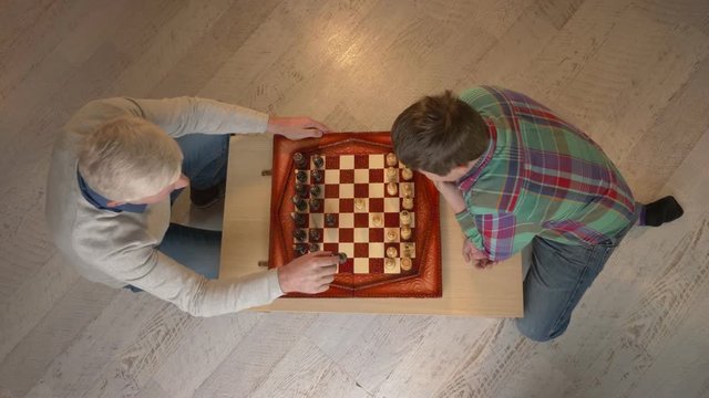 Grandfather and grandson plays chess. Elderly man teaches chess to play a young fat child. Home comfort, family idyll, cosiness concept, difference of generations, top shot. 60 fps