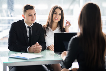 Saleswoman talking with a couple of happy customers sitting in a desktop at office. Manager consalting couple in office.