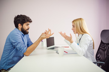 Cheerful young doctor listening to a patient in the office. Doctor talking with patient.