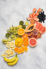 Above view of healthy fruits in rainbow colours, strawberries, mango, grapes, bananas, grapefruit on the off white table, vertical, copy space for text, selective focus