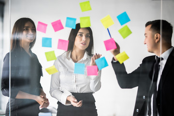 Three businesspeople discussing and planning concept. Front of glass wall marker and stickers. Startup office.