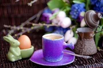 a bunch of spring flowers in lilac tones, and a cup of coffee with Easter bread and eggs, Easter