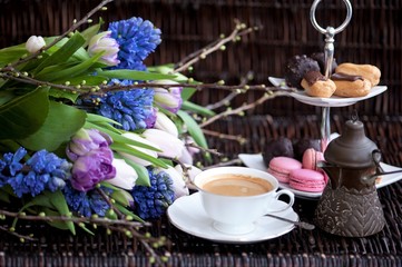 a bouquet of spring flowers in lilac tones and a cup of coffee with cakes