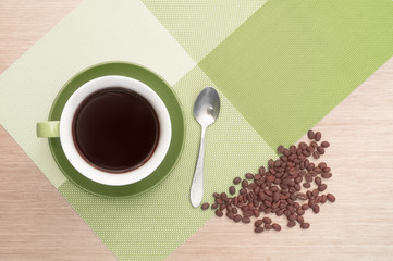 Green cup of coffee on the table background and tablecloth and beans and spoon