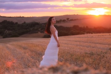 Fototapeta na wymiar an Asian woman in white dress in a field in Tuscany, Italy under sunset