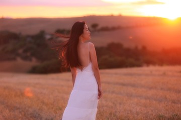 Fototapeta na wymiar a Asian woman in white dress in a field in Tuscany, Italy under sunset 