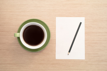 A green cup of coffee on the background of a table and a white shee and pencil