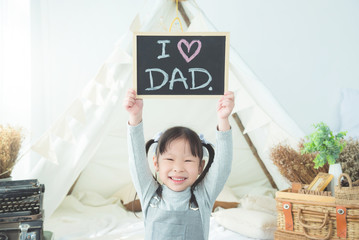 Little asian girl smiling while holding blackboard with text "I love dad"