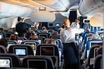 Naklejka premium Wnętrze dużego samolotu komercyjnego z pomocnikami lotniczymi obsługującymi pasażerów podczas lotu. Stewardesy w ciemnoniebieskim mundurze idącym do ołtarza. Skład poziomy.