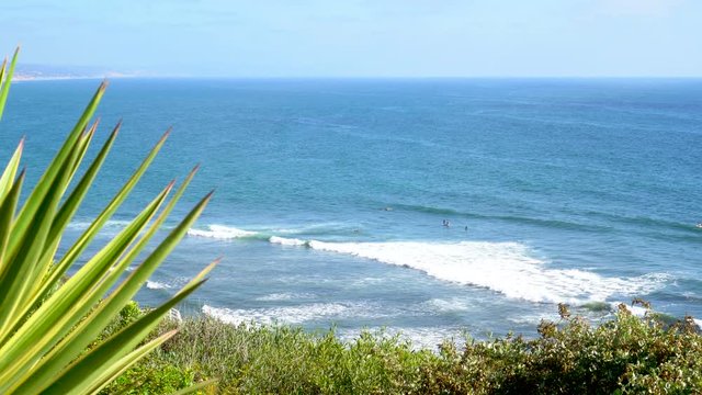 4K cliff side view of Encinitas Swami's beach in Southern California. Surfers swimming and riding waves.