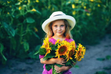 Beautiful little girl in a white wide-brimmed hat with flowers sunflower