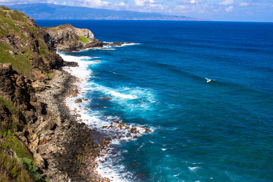 Volcanic rock, surf, and shades of the blue Pacific Ocean on the Maui coast, with the island of Molokai in the background