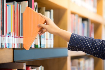 male hand choosing and picking orange book in public library, education research and self learning...