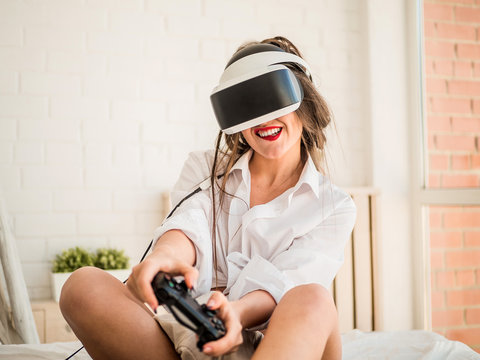 Young female gamer in wearable VR headset playing action 3d video game at home, excited teen holding wheel and screaming driving digital racing car in simulator application, virtual gaming concept