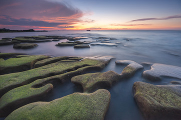 Obraz premium colorful sunset seascape with natural coastal rocks covered by green moss at Kudat Sabah Malaysia. 