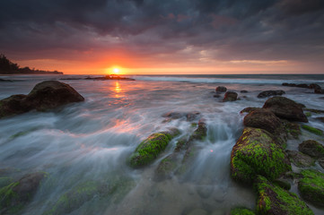 Naklejka premium vibrant sunset color with beautiful rocks formation covered by green moss. image may contain soft focus due to long expose.