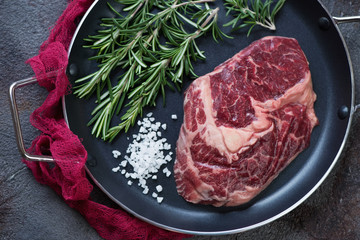 Above view of a frying pan with raw fresh free range beefsteak and seasonings, horizontal shot
