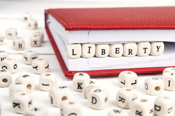 Word Liberty written in wooden blocks in notebook on white wooden table.
