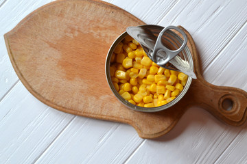 The tin with canned corn on the wooden cutting board. 