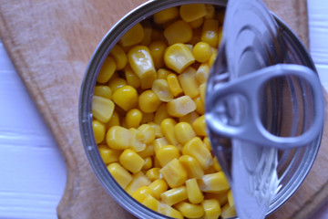 The tin with canned corn on the wooden cutting board. 