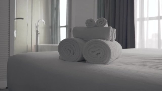 Freshly laundered fluffy towel rolls on a hotel bed in luxury hotel room with white bedding. Welcome resort decor in slow motion.