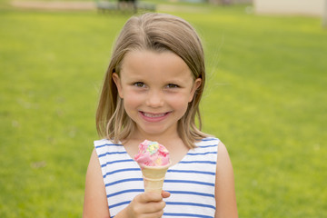 adorable and beautiful blond young girl 6 or 7 years old eating delicious ice cream smiling happy isolated on green grass field background