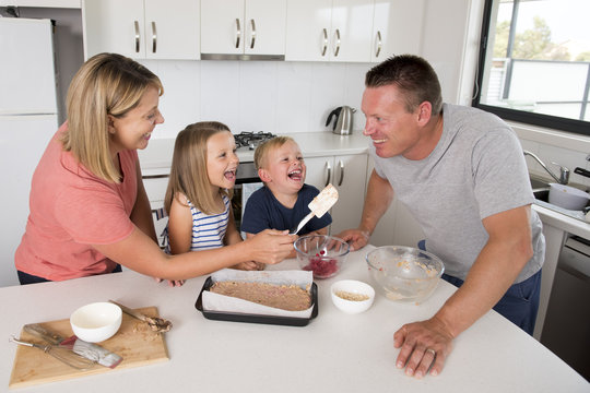 young happy couple baking together with little son and young beautiful daughter at home kitchen having fun playing with cream
