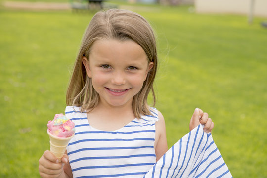 adorable and beautiful blond young girl 6 or 7 years old eating delicious ice cream smiling happy isolated on green grass field background