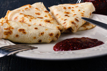 Stack of american pancakes or fritters with strawberry and blueberry jam in white plate on wooden rustic table