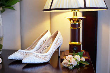 Wedding attributes of the bride. Beautiful and delicate white shoes with boutonniks and a ring