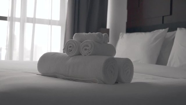 Freshly laundered fluffy towel rolls on a hotel bed in luxury hotel room with white bedding. Welcome resort decor in slow motion.