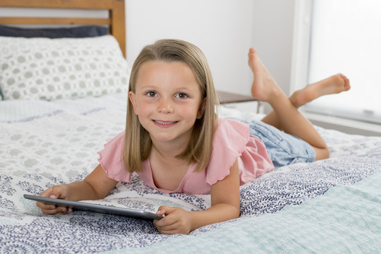 sweet and beautiful blond 6 or 7 years old young girl lying on bed smiling happy using the internet on digital tablet pad watching and having fun