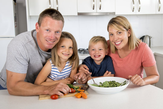 young attractive couple mother and father preparing salad together with little son and young beautiful daughter in healthy vegetable nutrition
