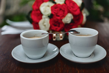 wedding bouquet and coffee with the wedding rings on the table