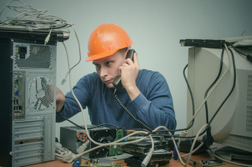 Computer repairman is talking on phone handset and is installing a new computer component. PC...