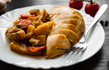 Fried chicken breast with carrots, onions and potatoes served on a white plate on dark wooden background