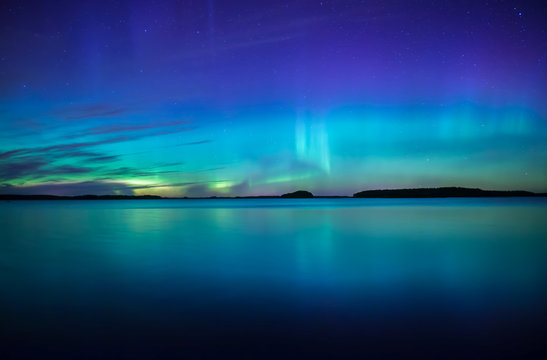 Northern lights dancing over calm lake. Farnebofjarden national park in Sweden