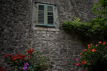 Fototapeta na wymiar Green broken window on old stone house decorative whit flowers