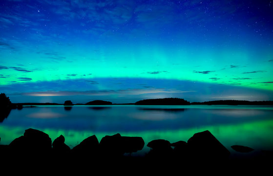 Northern lights dancing over calm lake. Farnebofjarden national park in Sweden.