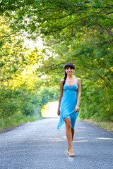 Fototapeta na wymiar Beautiful young brunette woman walking on the empty road at summer day