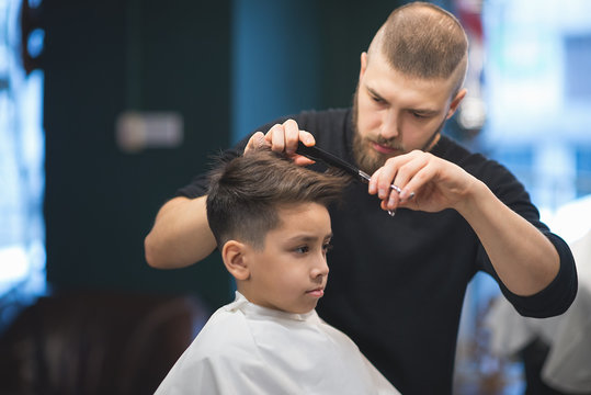 the young man the hairdresser cuts the schoolboy in hairdressing salon